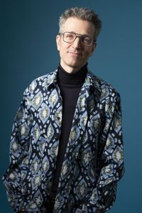 Wolfgang Kogert Portrait 2025 in gemustertem Hemd vor blauem Hintergrund