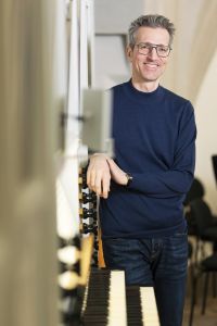 Wolfgang Kogert Portrait 2025 lehnend an der Orgel der Wiener Hofburgkapelle